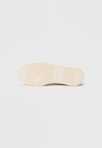 Krém színű sneaker talp textúrázott mintával és logónyomattal. Lekerekített forma sima felülettel, a tapadás érdekében tervezve.