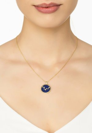 Gold necklace with a round pendant featuring a blue background and star constellation design in a gold outline. Chain is delicate and thin.