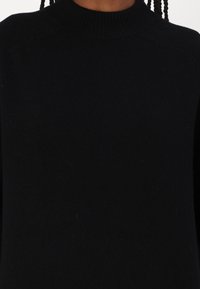 Maglione nero a collo alto lavorato a maglia, con colletto e polsini a coste, caratterizzato da una texture liscia e un design aderente. Nessun motivo o accento visibile.