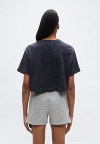 Κοντομάνικο κοντό μπλουζάκι σε ναυτικό μπλε χρώμα, με απαλό ύφασμα, συνδυασμένο με ανοιχτό γκρι σορτς. Απλός σχεδιασμός, χωρίς ορατά μοτί βα ή μεταλλικά στοιχεία.