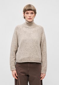 Beige pletený rolák s texturovaným povrchem, žebrovaným límcem a spadlými rameny. Má volný střih a rovný dolní lem.