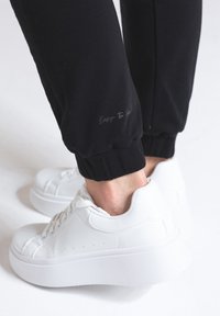 Czarne dresy z elastycznymi mankietami, z dyskretnym napisem "Łatwe do wyglądania", w zestawieniu z białymi sportowymi sneakersami na platformie.