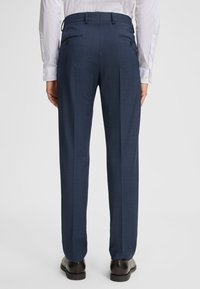 Marineblaue maßgeschneiderte Hose mit strukturiertem Muster, flachem Bund und zwei Gesäßtaschen. Kombiniert mit einem weißen Hemd und schwarzen Schuhen.