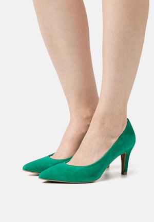 Zapatos de tacón alto de ante verde con punta puntiaguda y tacón moderado. El diseño presenta una textura suave y una parte superior baja para un aspecto elegante.