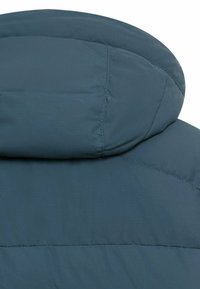 Gepolsterte Jacke mit hohem Kragen, aus glattem tiefgrünem Stoff. Verfügt über Steppnähte und einen leicht abgerundeten Ausschnitt für mehr Wärme.