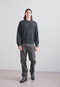 Dark green knitted sweater with a round neck and ribbed hem, paired with gray denim jeans and black ankle boots. Simple design and fit.