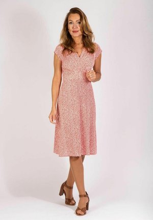 Rotes Blumenkleid mit kurzen, überzogenen Ärmeln, tailliertem Oberteil und ausgestellt geschnittenem, knielangem Rock. Kombiniert mit braunen Riemchensandalen. Glatte Stoffoberfläche.