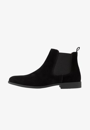 Boots Chelsea en daim noir avec des panneaux latéraux en élasthanne, un bout arrondi lisse et une semelle en caoutchouc noir basse. Équipées d'une languette à l'arrière pour un enfilage facile.