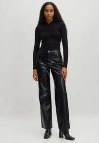 Zwarte lange mouwen top met een gewikkeld ontwerp, gecombineerd met hooggewaisted glanzende zwarte neplederen broek met een krokodillenpatroon. Zwarte hakken.