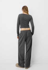 Grå långärmad crop top kombinerad med lösa grå sweatpants, med en elastisk midja och en bakficka, bärs med ljusa skor.