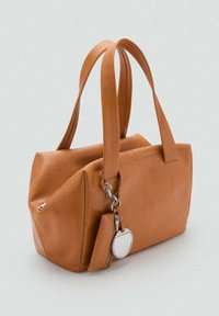 Tan leren handtas met dubbele hengsels, een klein ritspocketje en een ronde zilveren sleutelhanger aan de voorkant bevestigd.