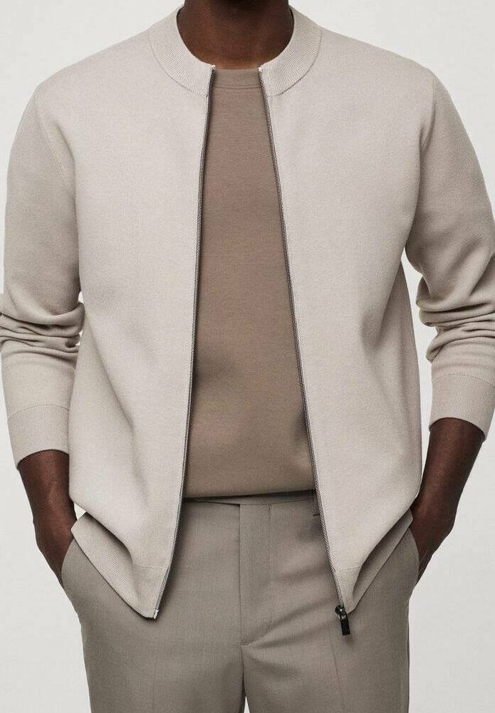 Cárdigan beige claro con cremallera y cuello redondo, combinado con una camisa beige. Presenta puños acanalados y un diseño elegante.