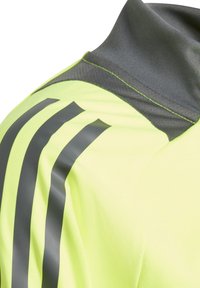 Korte mouwen sportshirt in felgeel met een grijze kraag. Kenmerkt zich door drie donkergrijze strepen op de schouder. Glad, lichtgewicht stof.