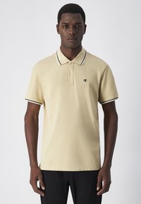 Polo shirt in lichtbeige met een kraag en zwart-witte gestreepte accenten. Bevat een klein logo op de borst en heeft korte mouwen.
