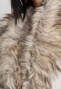 Estola de piel sintética en tonos variados de beige y marrón. Texturizada con fibras largas y onduladas, presenta una superficie suave y aterciopelada.