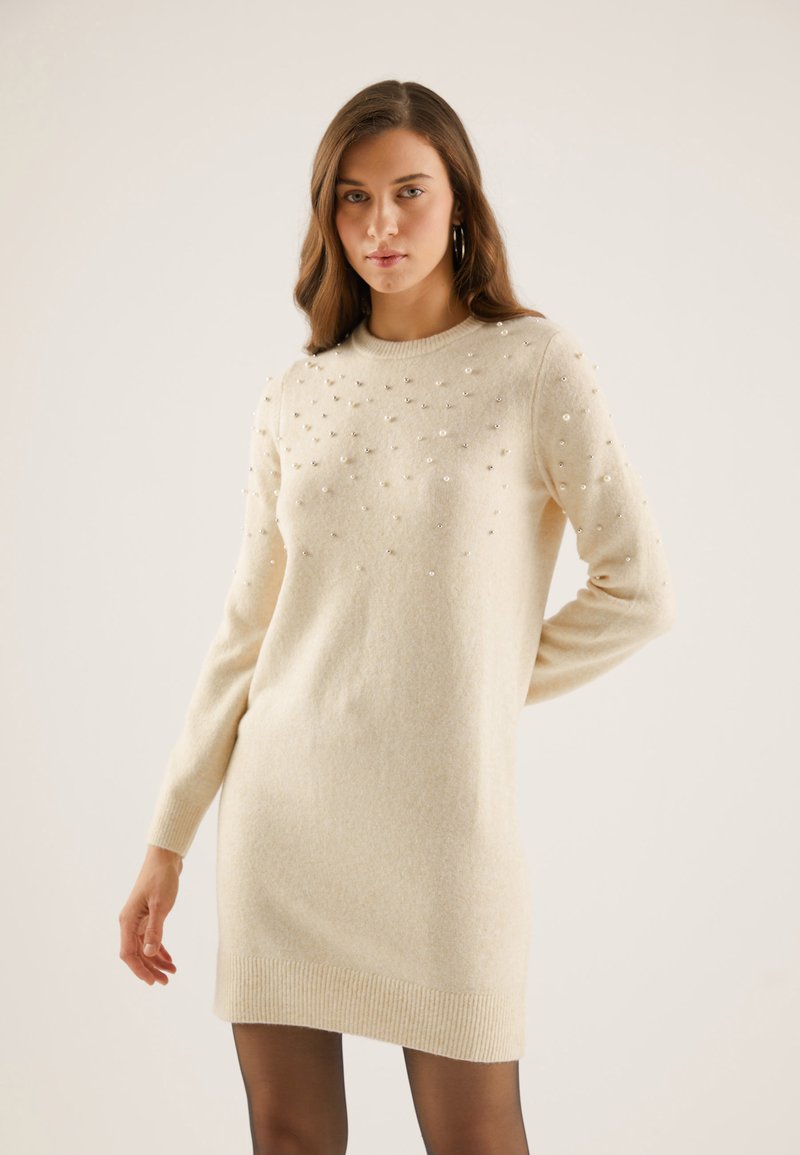 Light beige knitted sweater dress with a crew neck, embellished with metallic beads on the upper front, and ribbed cuffs and hem.