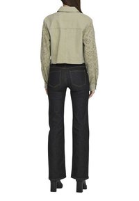 Veste en denim beige coupée avec des manches à motifs, associée à un jean droit bleu foncé et des escarpins noirs.