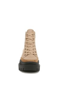 Beige high-top shoe with a canvas upper, suede accents, and a black rubber sole. Features metal eyelets and a textured lace-up design.