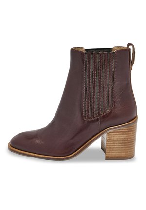 Bottine en cuir marron avec un bout pointu, des panneaux élastiques verticaux et un talon en bois empilé. Texture lisse avec une finition brillante.