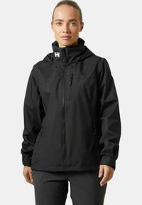 Chaqueta impermeable negra con capucha, cremallera frontal y bolsillos con cremallera, diseñada con un acabado mate suave y puños ajustables.