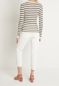 Schwarz- und cremefarbener gestreifter Ripppullover mit langen Ärmeln, kombiniert mit weißen strukturierten cropped Hosen und rosa Blockabsatzsandalen.