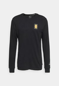 Langärmliges schwarzes T-Shirt aus Baumwolle. Verfügt über einen kleinen, farbenfrohen Grafikdruck auf der Brust und gerippte Manschetten.