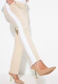 Beige kalhoty s bílým texturovaným proužkem po stranách, doplněné nahými lodičkami na vysokém podpatku s zlatým akcentem na podpatku.