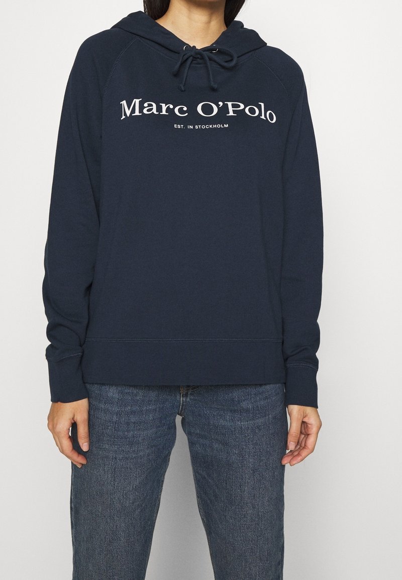 Granatowa bluza z kapturem ze sznurkiem, logo "Marc O'Polo" z przodu, ściągacze na mankietach i dole, wykonana z miękkiej bawełny.