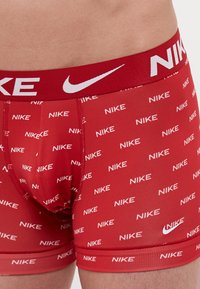 Czerwone bokserki Nike mają elastyczny pas z powtarzającym się białym napisem "Nike" oraz logo. Materiał jest gładki i przewiewny.