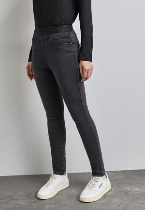 Jeans in denim nero slim fit con vita alta, dotati di tasche frontali e una superficie liscia. Abbinati a sneakers bianche.