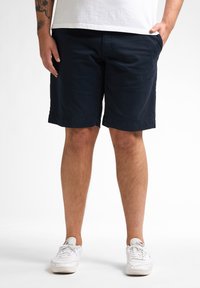 Navyblauwe shorts van katoen, met een recht gesneden pasvorm, zijzakken en een opgerolde zoom. Draagt met witte sneakers.