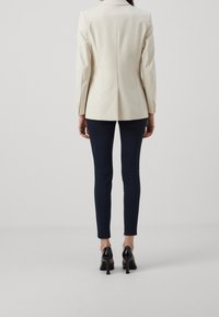 Blazer crema ajustado con hombros estructurados, combinado con pantalones navy de corte Slim y zapatos de tacón alto negros.