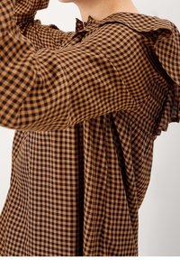 Blusa a quadri marrone e nera con collo arricciato e maniche lunghe, caratterizzata da un tessuto testurizzato. Il motivo è distribuito in modo uniforme.