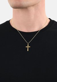 Collana con croce d'oro su una sottile catena, indossata sopra una maglietta nera a girocollo. La croce presenta un design semplice ed elegante.