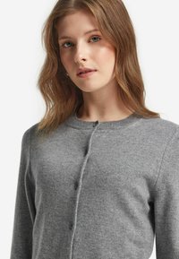 Grå stickad cardigan med rund halsringning, knappstängning och långa ärmar. Tyget har en mjuk textur med en slät yta.