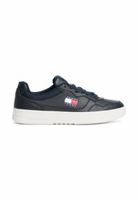 Navy leather sneakers with white sole, featuring Tommy Jeans logo patch in red, white, and blue. Rounded toe and flat lace-up design.