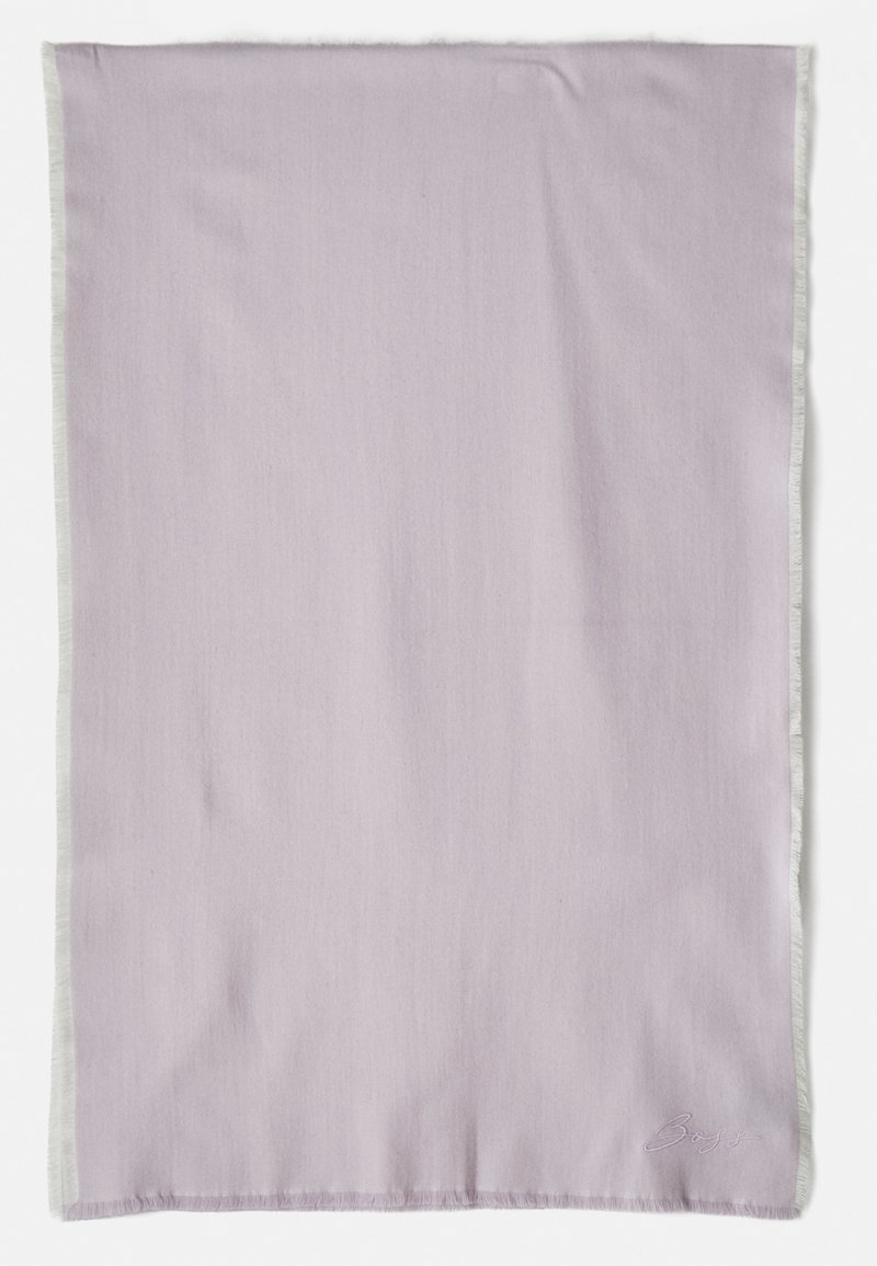 Light lavender soft fabric blanket with fringe edges; features subtle texture and embroidered branding in a matching color at the bottom right.