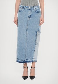 Denim midi krilo v svetlo modri barvi s ravno silhueto, opremljeno s cargo žepom in strganim robom, kombinirano s črnimi špicastimi petami.