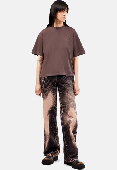 Camiseta de algodón marrón con un diseño corto, combinada con pantalones de cintura alta, con estampado en negro y beige, que presentan detalles texturizados y un ajuste holgado.