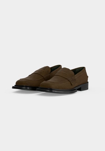 Ζευγάρι καφέ δερμάτινα penny loafers με μαύρες σόλες, με ραμμένο επάνω μέρος και χαμηλό τακούνι σε απλό ανοιχτό φόντο.