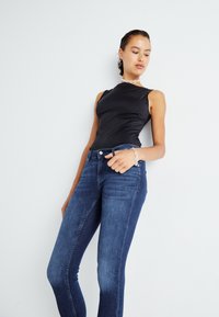 Un bodysuit negro sin mangas combinado con un ajustado jeans de mezclilla azul oscuro. Presenta una textura suave y un brillo sutil, con un diseño clásico de cinco bolsillos.