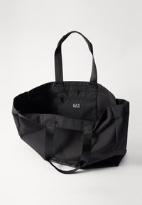 Borsa a spalla in tessuto nero con due manici robusti, ampio interno e una piccola tasca con zip. Dispone di una patch del logo interna.