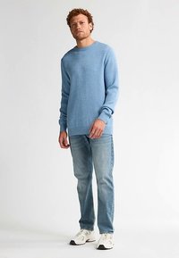 Lichtblauwe gebreide trui met een ronde hals en lange mouwen, gecombineerd met lichtblauwe spijkerbroek en witte sneakers. Casual pasvorm, zachte textuur.