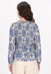 Bluse mit Blumenmuster und langen Ärmeln, aus einem leichten Stoff; in Blau- und Cremetönen gehalten, mit geraffter Taille und Schlüsselaugen-Rücken.