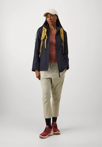 Ναυτικό μπλε αδιάβροχο με κίτρινες λωρίδες, ροζ κορυφή, μπεζ παντελόνι μέχρι τον αστράγαλο, μαύρες κάλτσες και κόκκινα αθλητικά παπούτσια. Απλή, λειτουργική εξωτερική ένδυση.