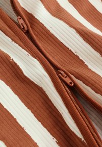 Lähivaade pruunide ja valgete triipudega soonik kangast, millel on vertikaalselt joondatud kaks pruunist luku tõmbelehte.