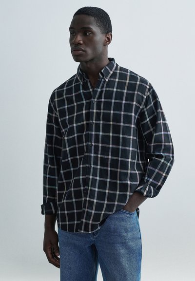 Chemise à carreaux noire et multicolore avec manches retroussées, col boutonné et tissu doux ; associée à un jean en denim bleu.