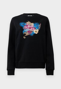 Crna dukserica s vibrantnim cvjetnim, leopard uzorkom i zlatnim lancem, s natpisom "Just Cavalli" na prsima.
