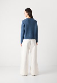 Blauwe gebreide trui met een cropped fit, ronde halslijn en geribde zoom. Gecombineerd met loszittende, lichtgekleurde broeken. Minimalistisch ontwerp.