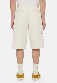 Shorts beiges arrivant au genou, avec un devant plat, des passants de ceinture, deux poches arrière et une poche cargo, fabriqués dans un tissu lisse.